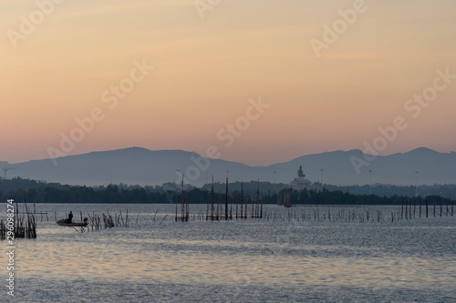 View of the lake with soft morning light , colorful sky, Buddhist statue view from distance and mountains in background.