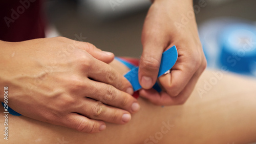Sports injury kinesio treatment. therapist placing kinesio tape on patient's knee