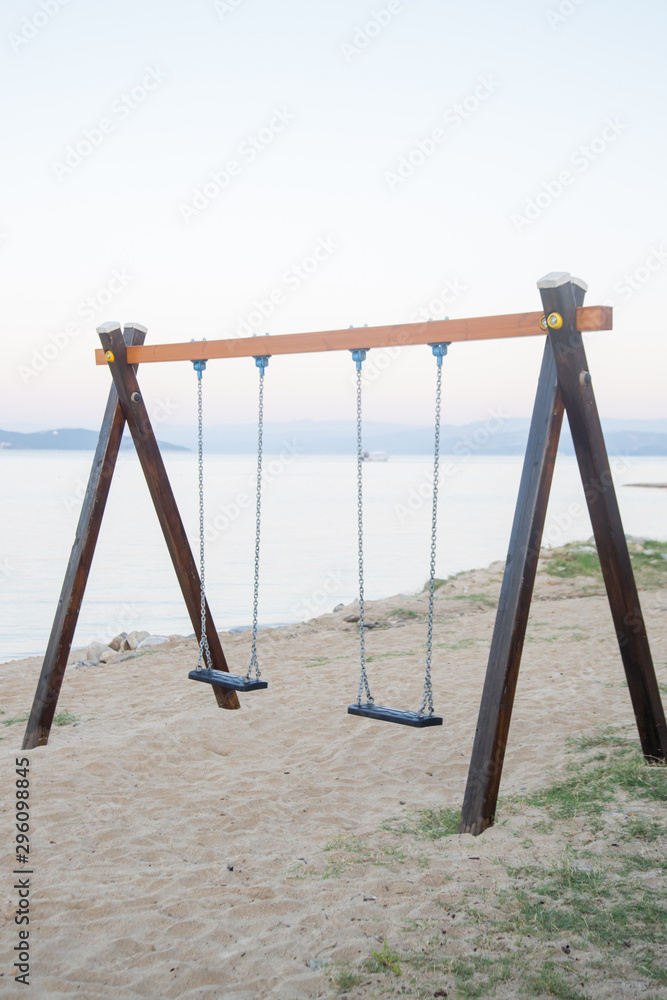 Fototapeta premium Simple children's wooden swings on an empty sandy beach