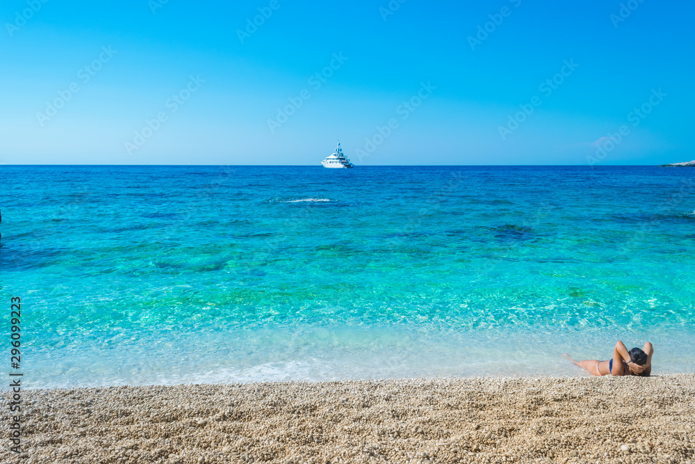 A girl is lying on the beach enloying the view of turquoise waters of the ocean at Petani beach in Kefalonia, Greece A girl is lying on the beach enloying the view of turquoise waters of the ocean at Petani beach in Kefalonia, Greece