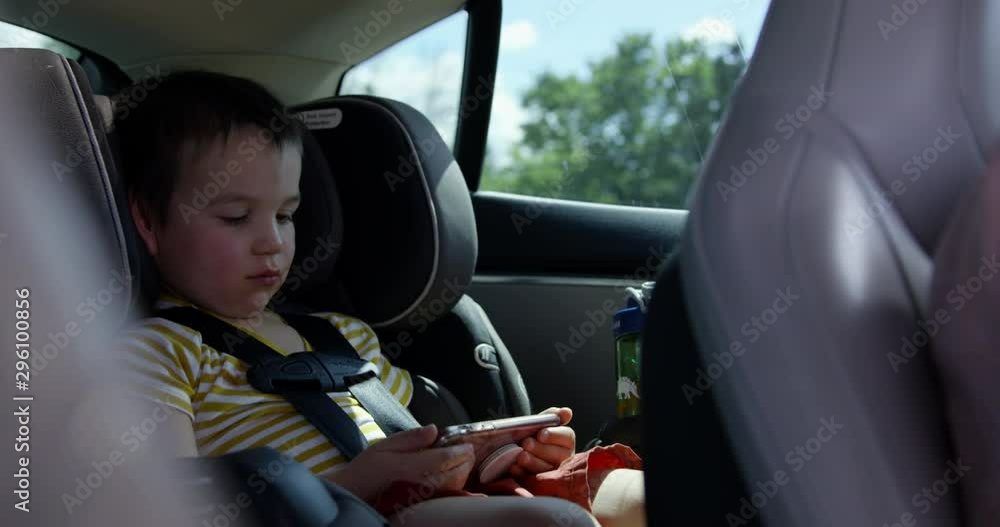 Toddler boy in carseat glued to smart phone on family road trip - addicted children Toddler boy in carseat glued to smart phone on family road trip - addicted children