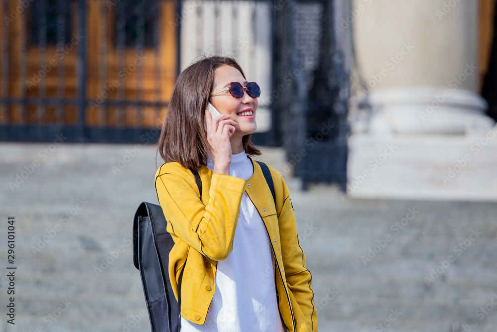 Fototapeta premium Portrait of a young, attractive and beautiful Asian woman smiling as she talks on her smartphone int he city. She is looking away as she talks animatedly and happily on her mobile device.