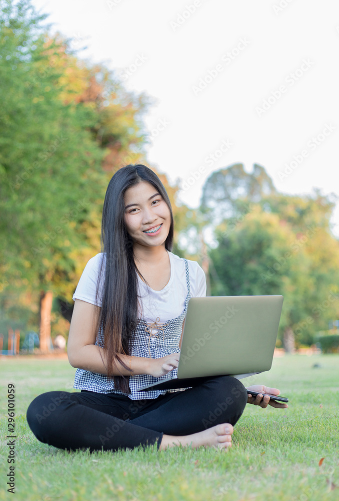 An Asian woman sat on the lawn and held with a smiling laptop face. An Asian woman sat on the lawn and held with a smiling laptop face.