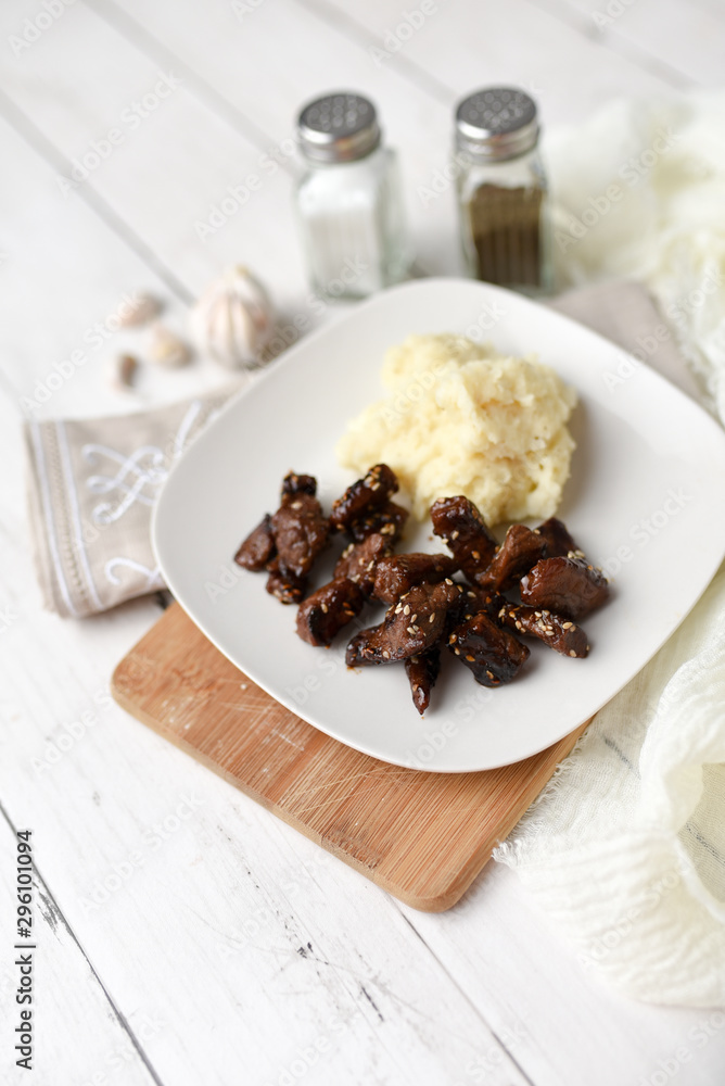 Sesame beef dish on a white wood background served with mashed potatoes and seasonings