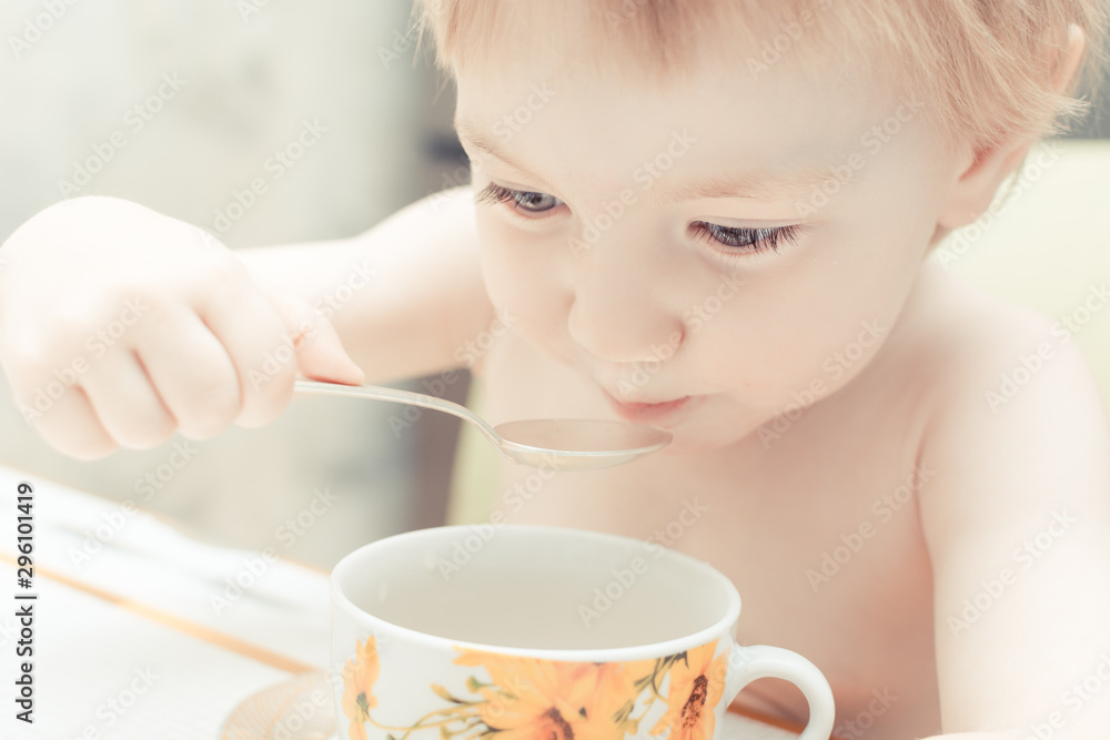 Cute child with blue eyes drinking tea from a spoon in the kitchen. Cute child with blue eyes drinking tea from a spoon in the kitchen.