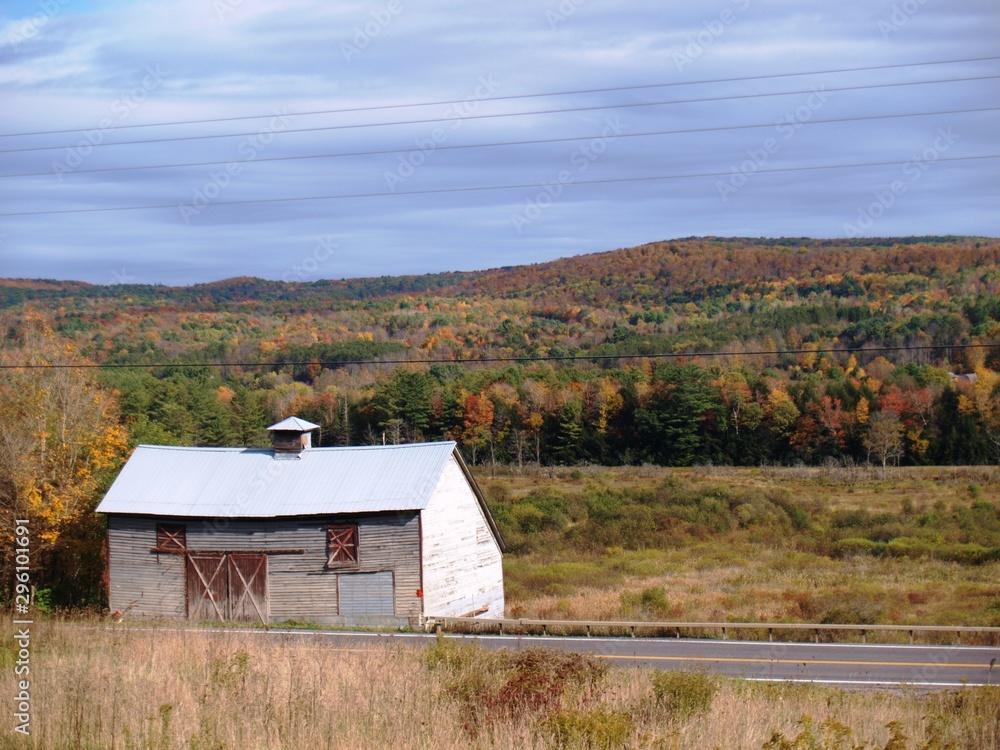 Old gray and red barn with autumn colors on the hills behind Old gray and red barn with autumn colors on the hills behind