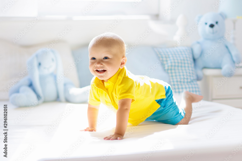 Baby boy playing on bed in sunny nursery Baby boy playing on bed in sunny nursery