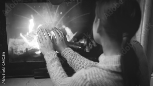 Black and white closeup image of woman sitting by the fireplace and warming her hands