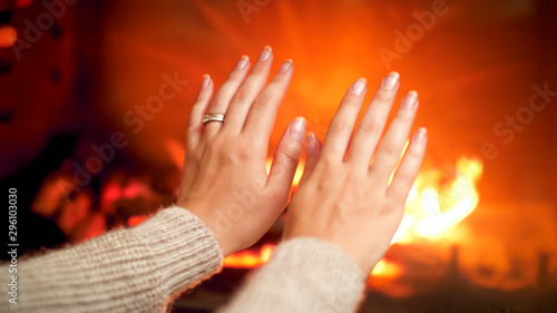 Closeup photo of woman with cold hands stretching them to the burning fireplace