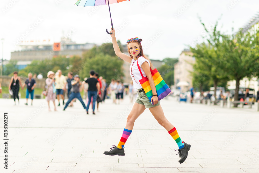 Lesbian in colorful lgbt socks and rainbow umbrella jumping at city square.