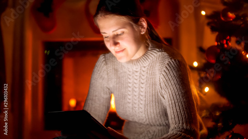 Portrait of young woman in sweater sitting next to the fireplace and using digital tablet