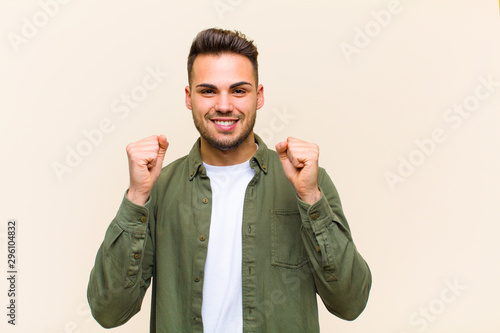 young hispanic man feeling shocked, excited and happy, laughing and celebrating success, saying wow! against isolated background photo