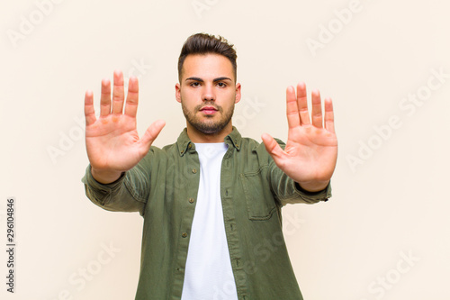 young hispanic man looking serious, unhappy, angry and displeased forbidding entry or saying stop with both open palms against isolated background photo