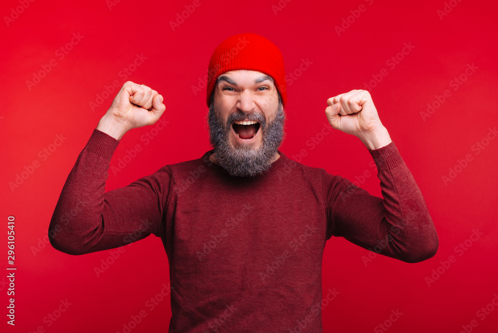 Portrait of cheerful man with white beard celebrating success over red background, winter theme Portrait of cheerful man with white beard celebrating success over red background, winter theme