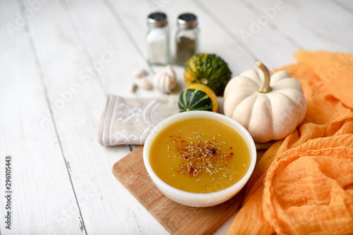 Pumpkin vegetable soup on white wooden backdrop and seasonings. Fall harvest soup 