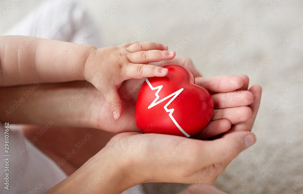 family, charity and health concept - close up of little baby and mother's hands holding red heart with ecg line family, charity and health concept - close up of little baby and mother's hands holding red heart with ecg line