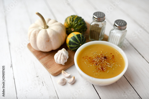 Pumpkin vegetable soup on white wooden backdrop and seasonings. Fall harvest soup 