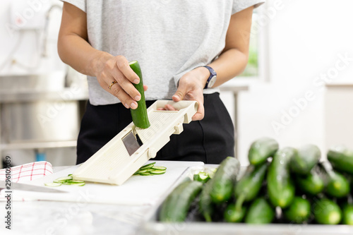 Woman slicing cucumber with vegetable slicer for salad. photo