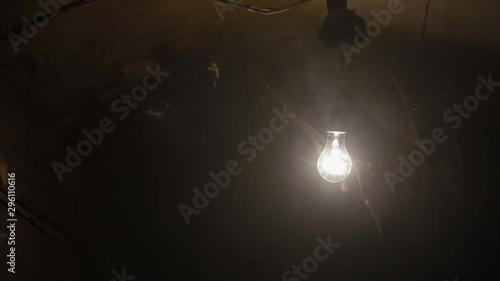 Close-up ordinary electric lamp hanging and swinging in dusty and smoky rusty and dirty basement bunker, like bomb shelter, huge spider web in foreground