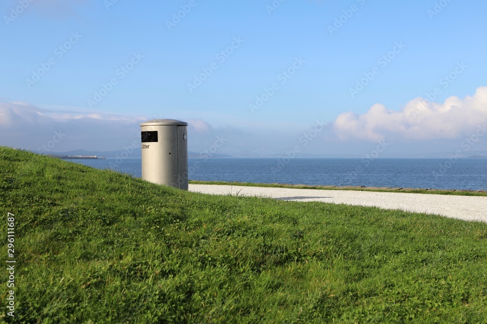 Litter bin overlooking coastline with green grass & blue sky