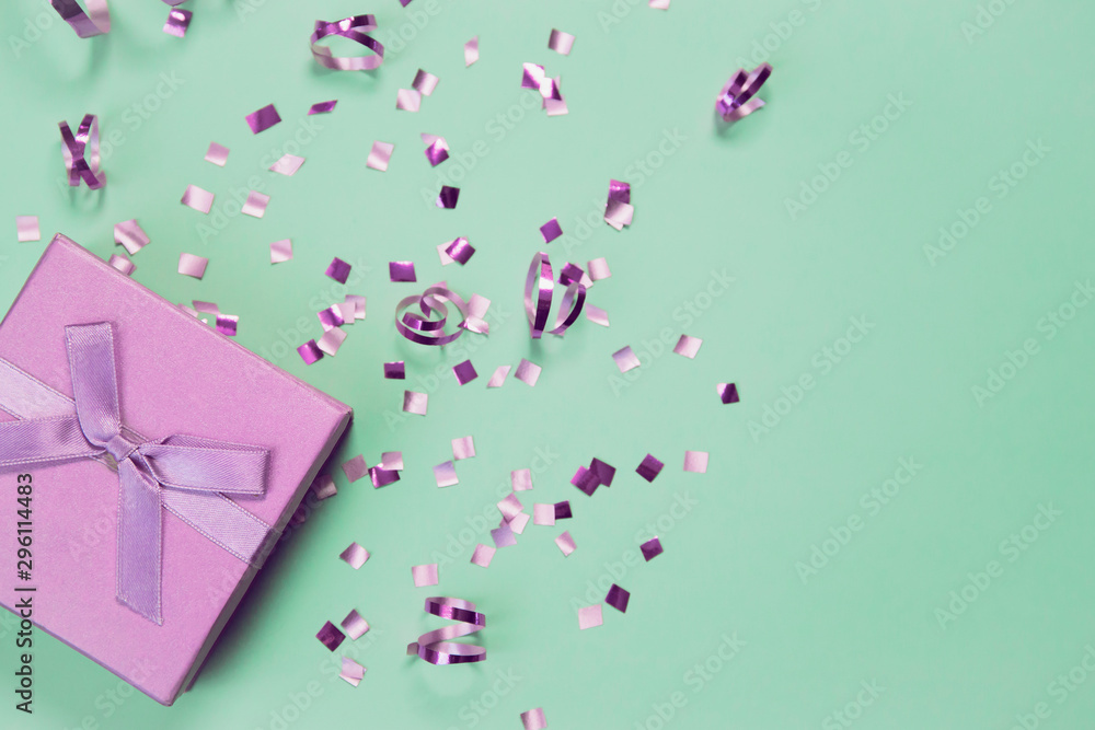 Present box on mint background with shiny confetti. Holiday and festive backdrop. Flat lay style