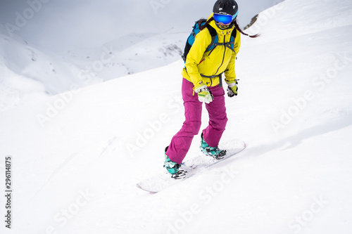 Sporty woman in helmet and mask snowboarding on snowy slope.