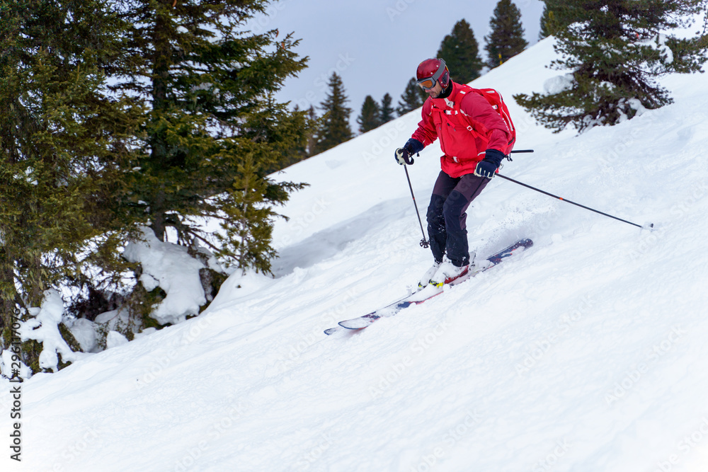 Side photo of sports man in red jacket and with backpack skiing in winter resort