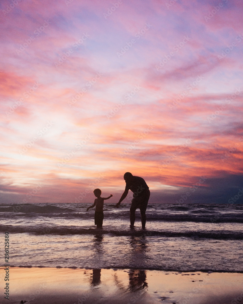 Father and son playing on the beach at the sunset time.