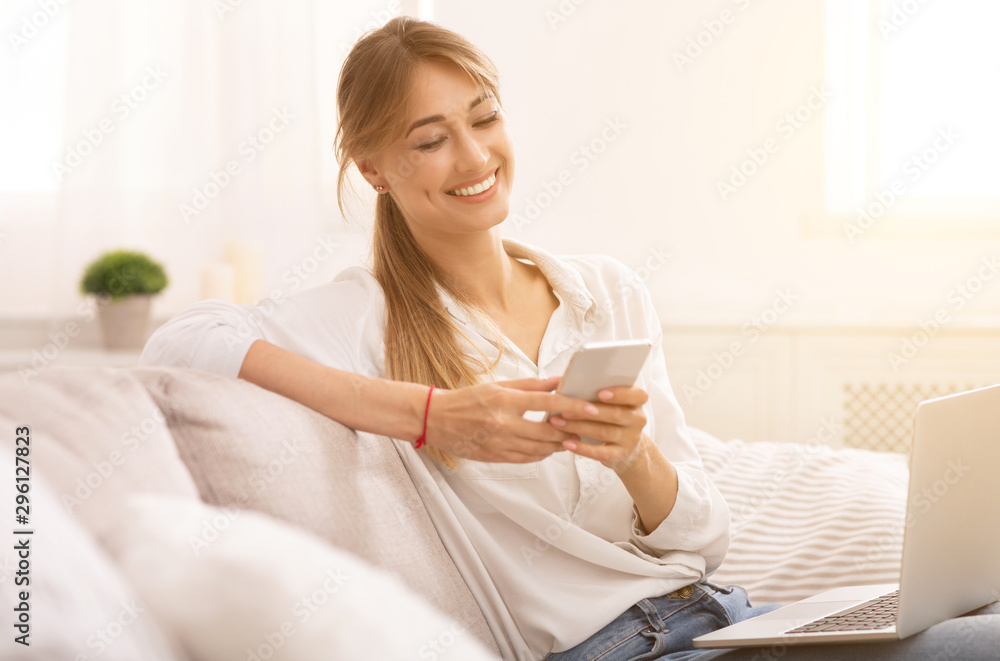 Relaxed Woman Using Smartphone Sitting With Laptop On Couch Indoor Relaxed Woman Using Smartphone Sitting With Laptop On Couch Indoor