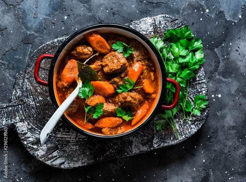 Cozy comfort winter autumn food - spicy braised crock pot beef in a pot on a rustic wooden board on a dark background, top view