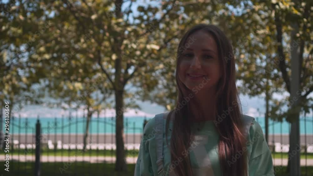 A girl in white shorts and a T-shirt with long hair walks along the city promenade. A girl walks among green trees on the promenade against the background of the sea. A girl in white shorts and a T-shirt with long hair walks along the city promenade. A girl walks among green trees on the promenade against the background of the sea.