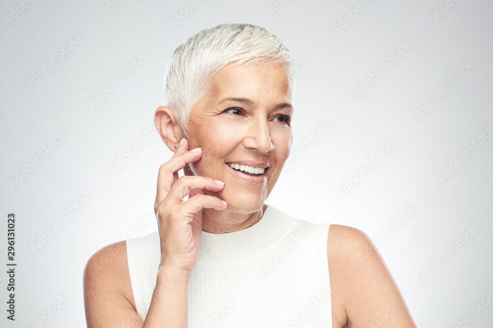 Beautiful smiling senior woman with short gray hair posing in front of gray background. Beauty photography. Beautiful smiling senior woman with short gray hair posing in front of gray background. Beauty photography.