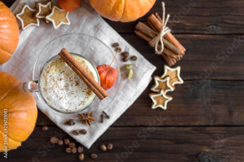 Pumpkin latte with cinnamon and spices in a glass glass on a wooden background. Pumpkins, cookies, spices and coffee. Autumn mood. Top view, copy space. Dark photo. Selective focus