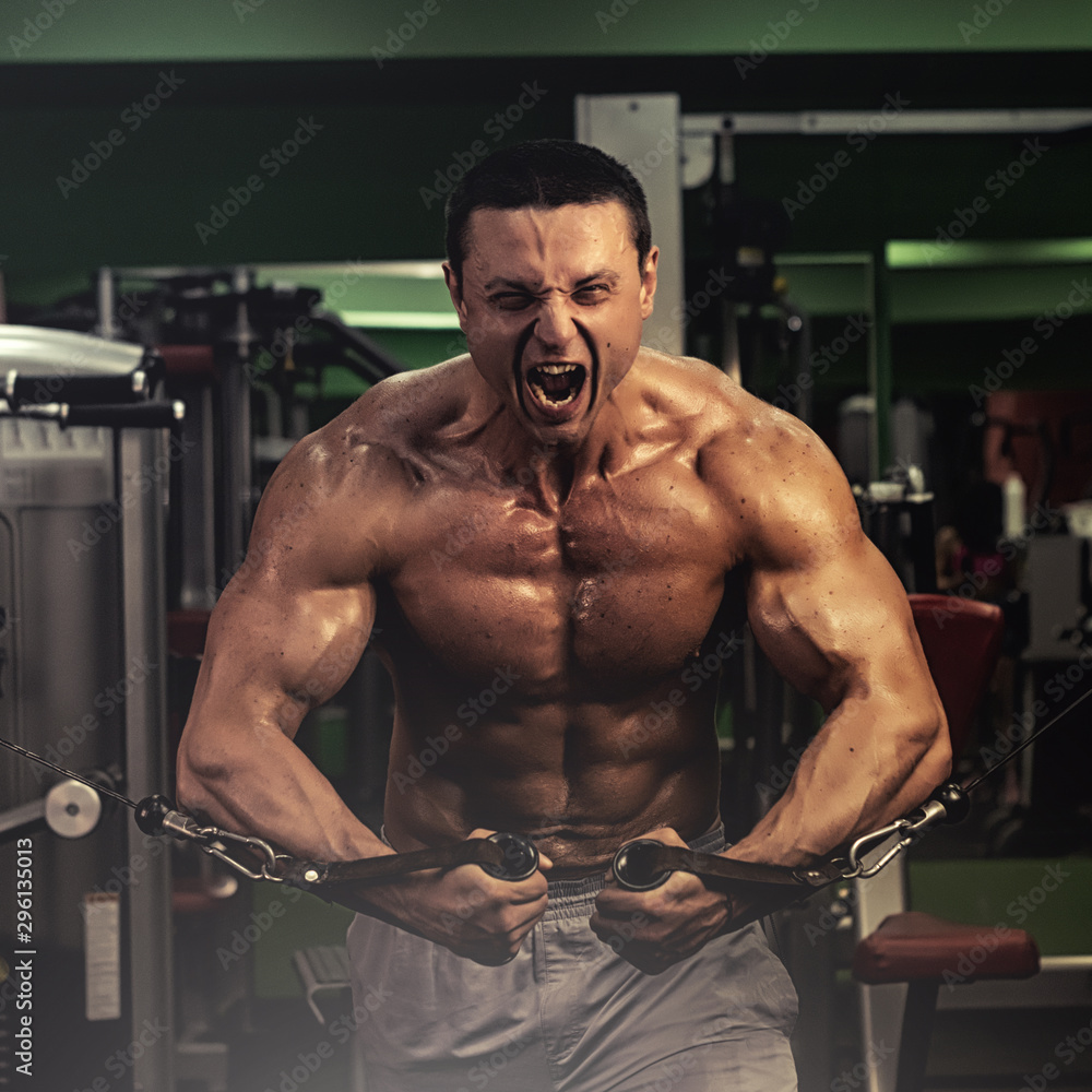 Fototapeta premium muscular bodybuilder doing exercise on bars in the gym. a handsome, sporty, sexy guy with a abs training in the gym. fitness, bodybuilding, nutrition, healthy lifestyle