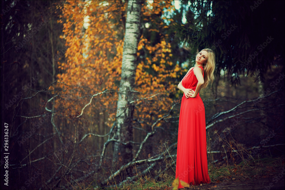 Outdoor fashion art photo of young beautiful blonde woman in long red dress surrounded autumn leaves outdoor in park. Autumn season fashion concept Outdoor fashion art photo of young beautiful blonde woman in long red dress surrounded autumn leaves outdoor in park. Autumn season fashion concept