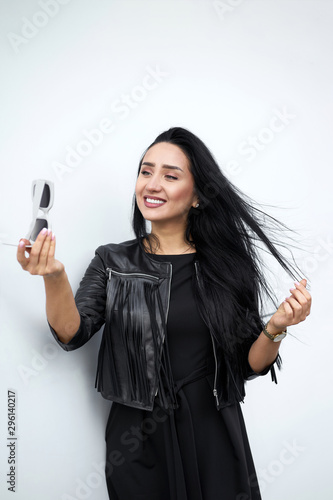 Urban style. Stylish girl with charming smile in modern sunglasses wearing elegant dress and fashionable black fringed leather jacket looking in reflection in sunglasses. Model in trendy outfit.