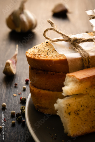 A stack of three croutons with ground pepper and one broken crouton in the foreground on a gray plate. The garlic in the background is blurred. Peppercorns on a dark wooden surface. Vertical orientati photo