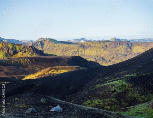 Three tents alone in Botnar campsite at Iceland on Laugavegur hiking trail, green valley in volcanic landscape among lava fields with view on Myrdalsjokull glacier. Early morning sunrise light