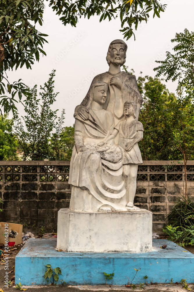 Bang Saen, Thailand - March 16, 2019: Wang Saensuk Buddhist Monastery. White stone Christian statue of Holy Family, Joseph, Mary and boy Jesus against silver sky and green foliage.