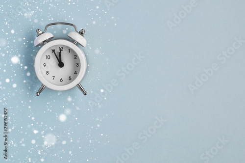 A cozy winter card with a small alarm clock under the snow on a blue mint background.