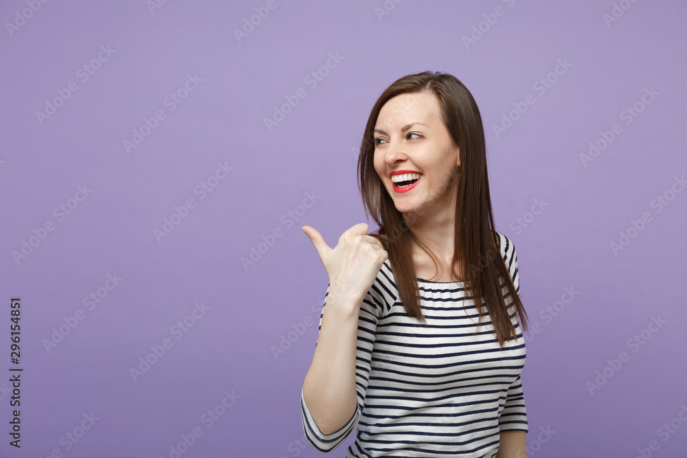 Laughing cheerful young brunette woman girl in casual striped clothes posing isolated on violet purple background studio portrait. People lifestyle concept. Mock up copy space. Pointing thumb aside. Laughing cheerful young brunette woman girl in casual striped clothes posing isolated on violet purple background studio portrait. People lifestyle concept. Mock up copy space. Pointing thumb aside.
