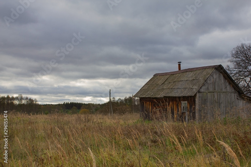 Autumn landscape with an old ruined wooden house. Old house in a field in the village on a cloudy day.