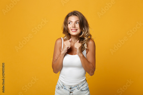 Excited young woman girl in light casual clothes posing isolated on yellow orange background studio portrait. People lifestyle concept. Mock up copy space. Looking aside, clenching fists, making wish.