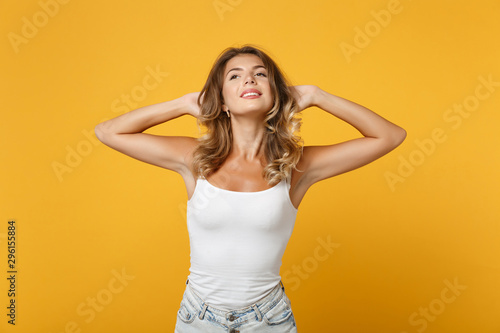 Relaxed smiling young woman girl in light casual clothes posing isolated on yellow orange wall background studio portrait. People lifestyle concept. Mock up copy space. Standing with arms behind head.
