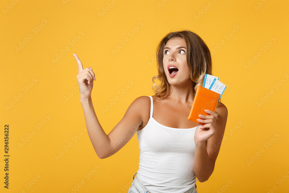 Shocked young woman girl in light casual clothes posing isolated on yellow orange background. People lifestyle concept. Mock up copy space. Point index finger up, hold passport, boarding pass, ticket. Shocked young woman girl in light casual clothes posing isolated on yellow orange background. People lifestyle concept. Mock up copy space. Point index finger up, hold passport, boarding pass, ticket.