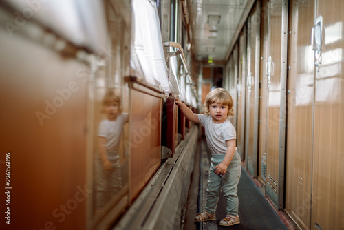 Cute blonde baby girl plays on the train, travels in a compartment car, runs a long corridor. Travel concept with kids.