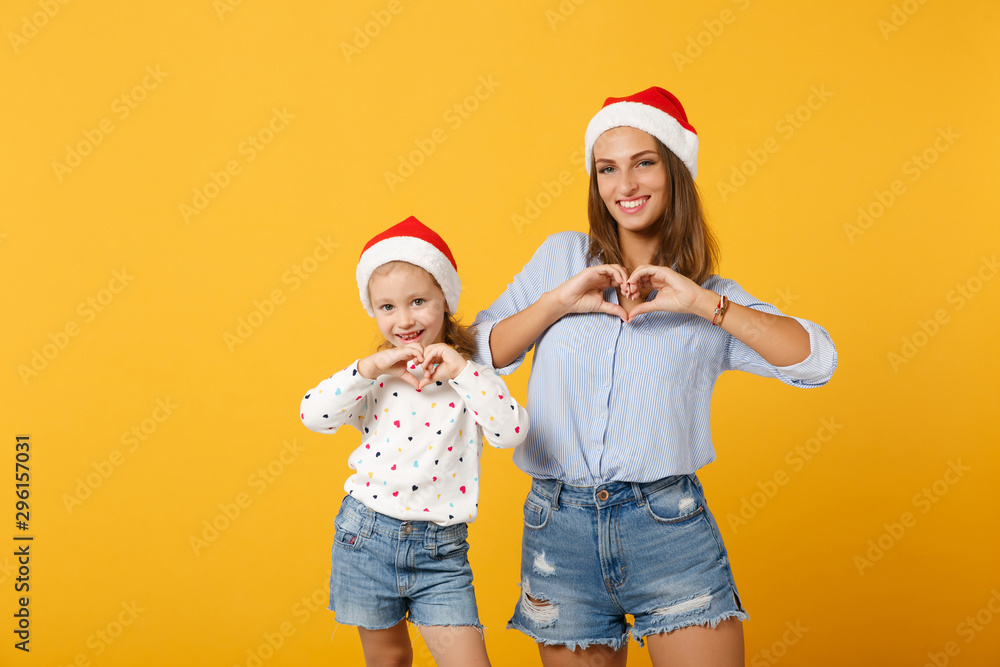 Fototapeta premium Woman child baby girl 4-5 years old in Christmas Santa hat. Mommy little kid daughter isolated on yellow background studio portrait. Happy New Year 2020 celebration holiday concept. Mock up copy space