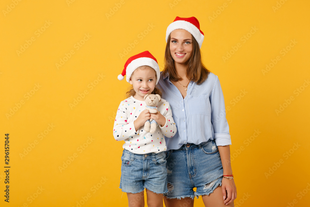 Obraz premium Woman child baby girl 4-5 years old in Christmas Santa hat. Mommy little kid daughter isolated on yellow background studio portrait. Happy New Year 2020 celebration holiday concept. Mock up copy space