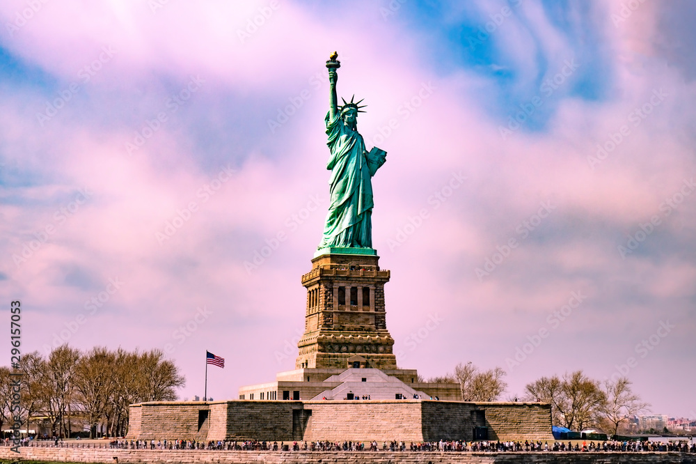 Fototapeta premium Statue of liberty with many tourists around it with pinky cloudy sky before sunset