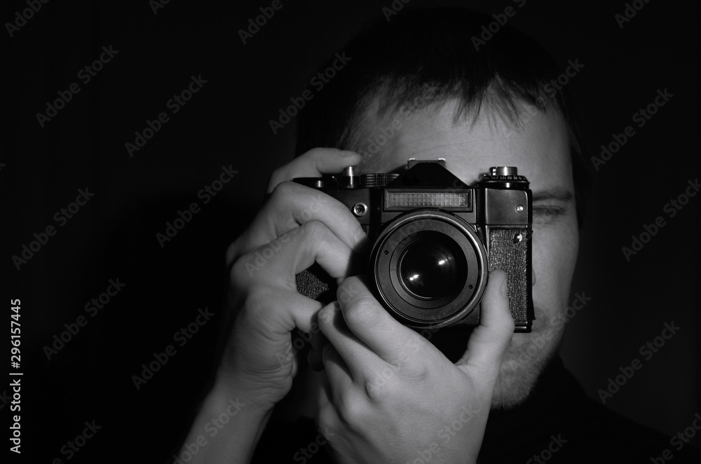 black and white portrait of a photographer with an old camera in his hands on a dark background.horizontal frame black and white portrait of a photographer with an old camera in his hands on a dark background.horizontal frame